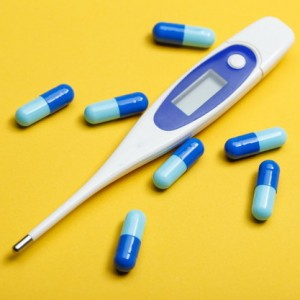 electronic thermometer and blue capsules on yellow background